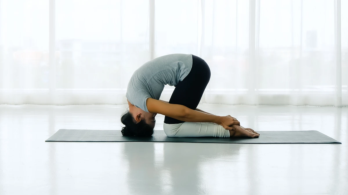 A young woman doing the sasangasana yoga pose in a bright white studio
